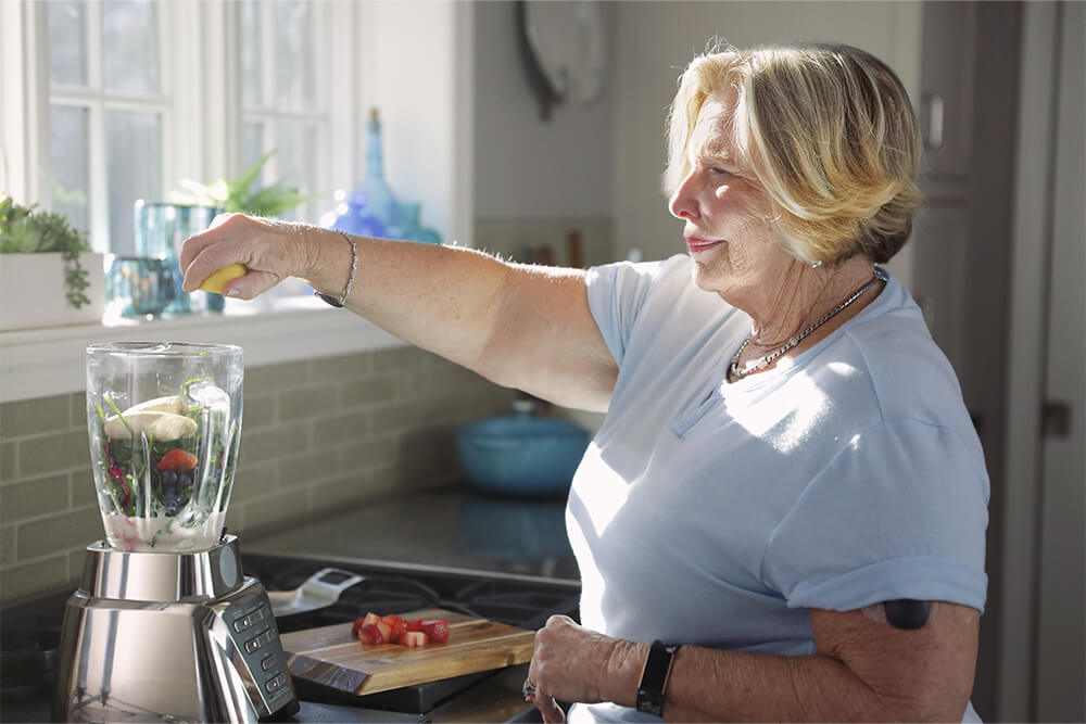 Donna che prepara un frullato mentre utilizza un dispositivo di monitoraggio continuo del glucosio.